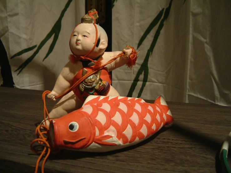 small doll posed on top of a large toy fish