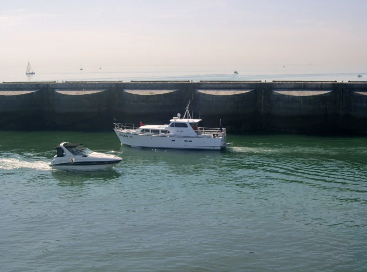 two boats pass by a large bridge while a speedboat is in the water