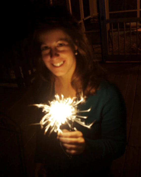 a woman standing up and smiling at the camera holding sparklers