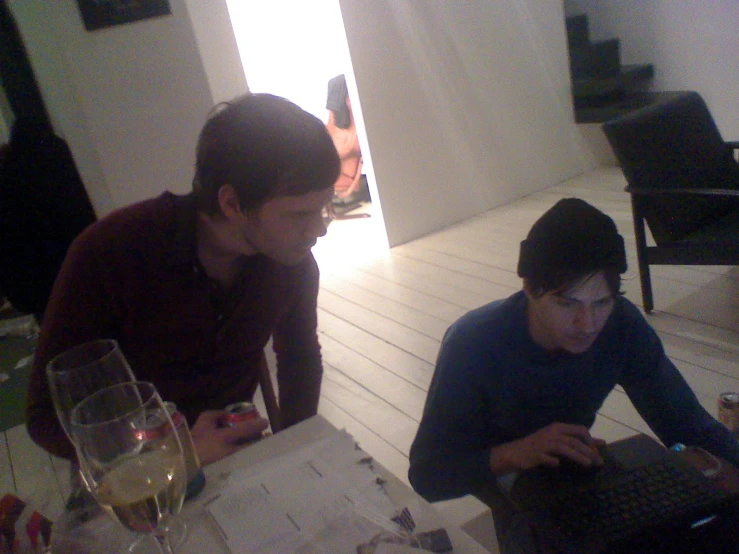 two men are using their laptops and a glass of wine