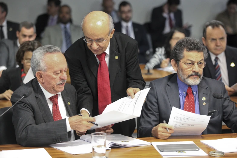 a group of men sitting around a table with paperwork in hand