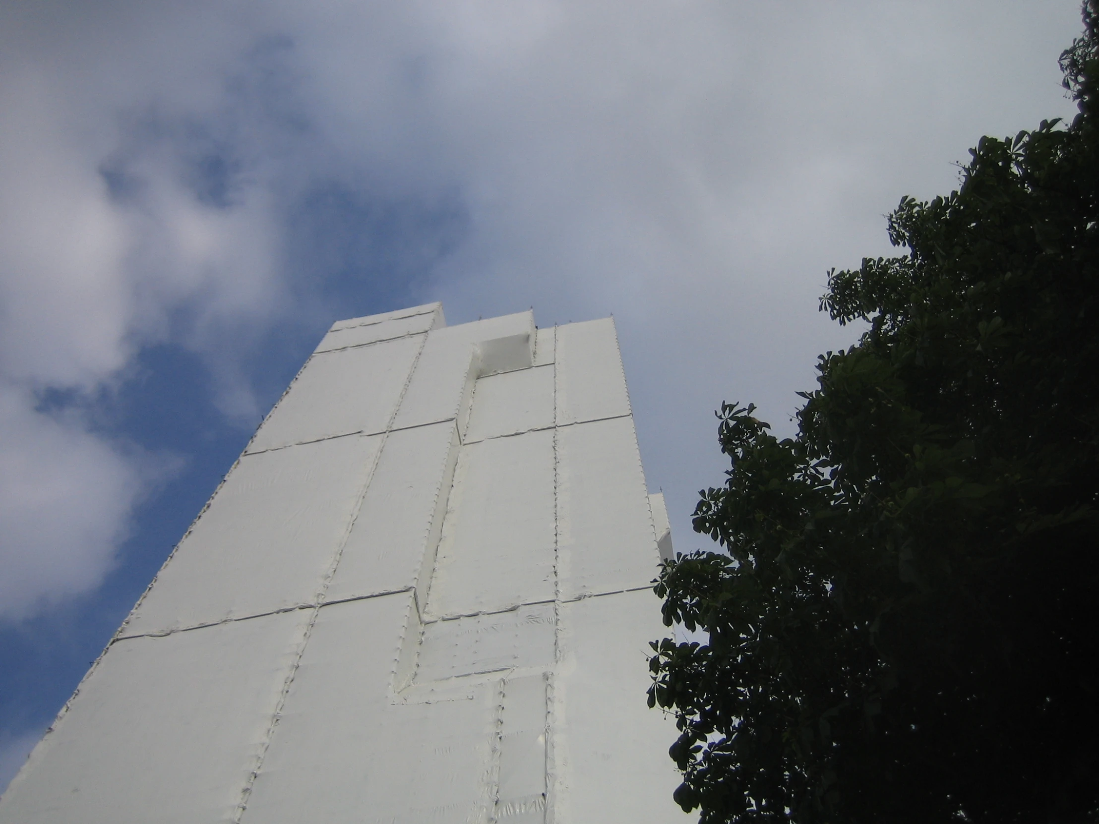 the top of a white building with a tree and cloudy sky in the background