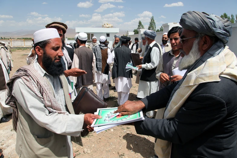 two men shaking hands with one another while other men in various colored dresses watch