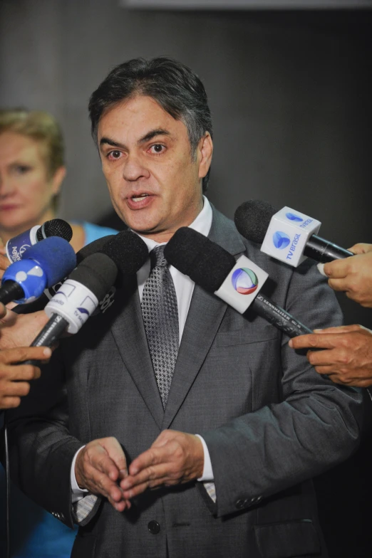 man in grey suit talking to reporters in a room