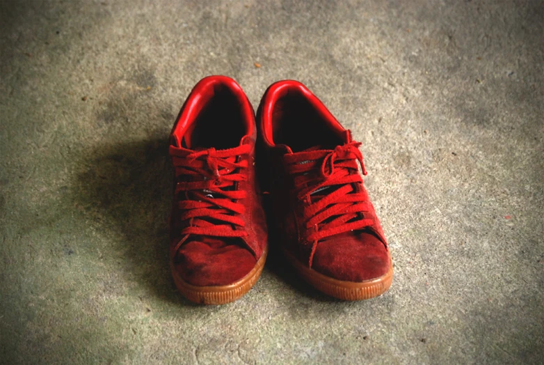 red shoes on a concrete floor and two pairs of red laces