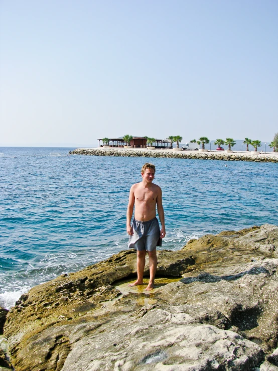 a man in boxers standing on top of a rock next to water