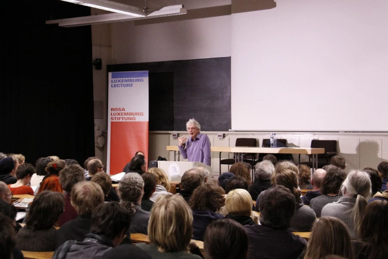 the woman is standing in front of a crowd in a lecture hall