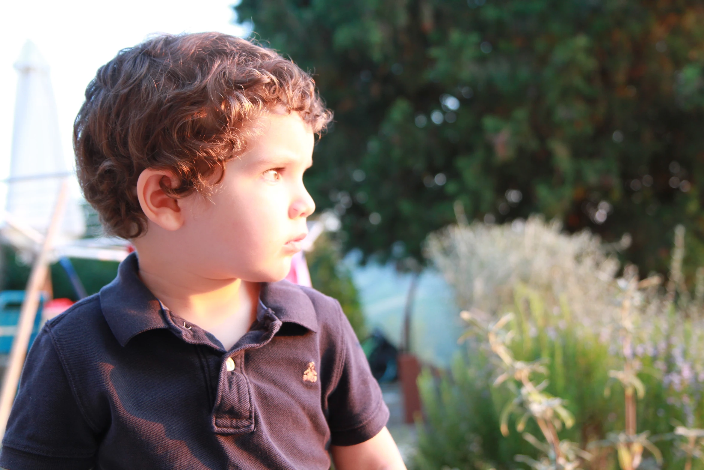 young child standing near grass and flowers with fence in background