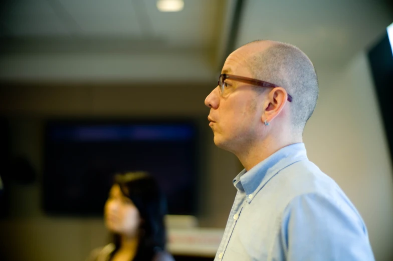 a man with bald hair and glasses stands in front of a television