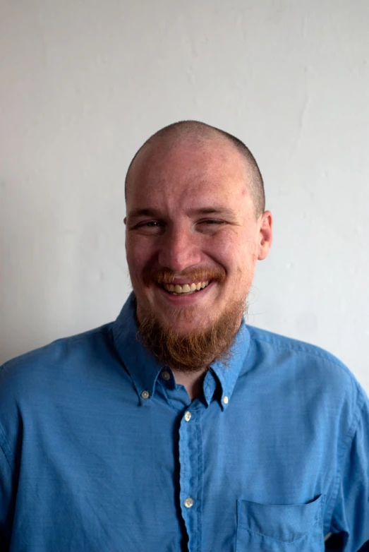 a smiling bearded man with a blue shirt on