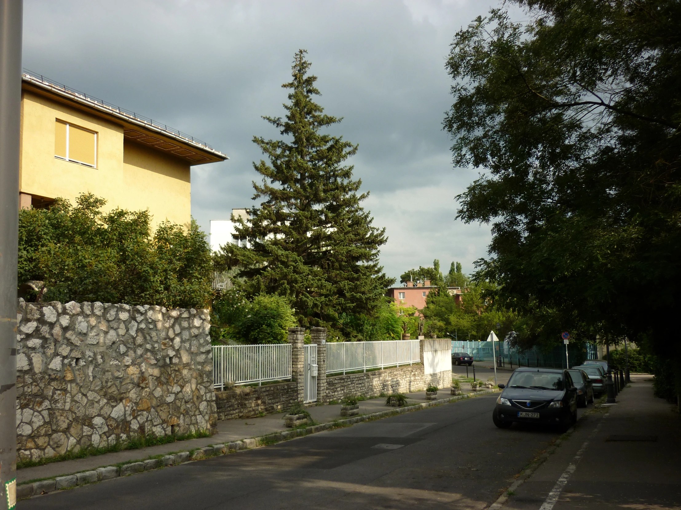 a stone fence surrounds a quiet street lined with cars