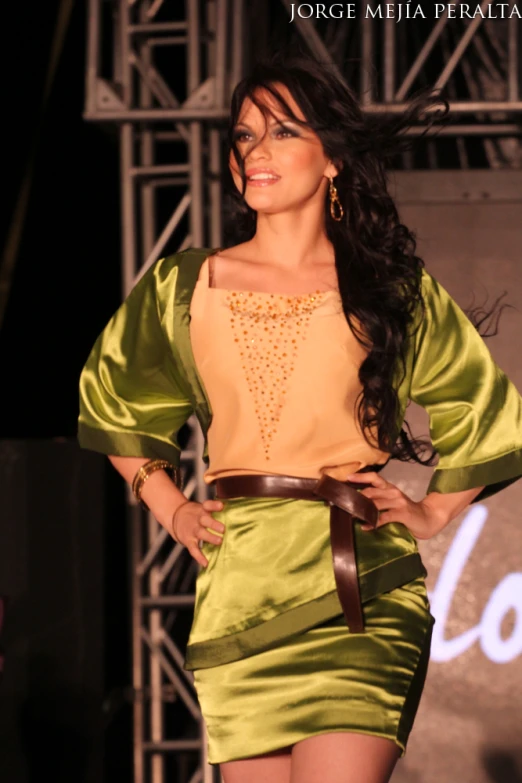 a woman with dark hair is dressed in a gold skirt and matching top