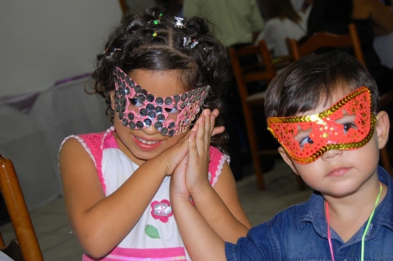 a pair of children wear bright red, gold and pink masks
