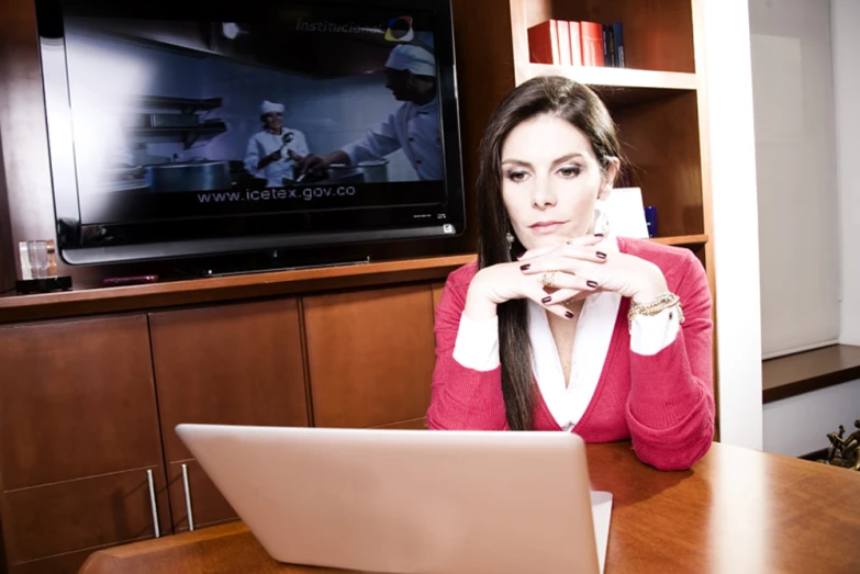 the woman sits in front of a television with her laptop on her lap