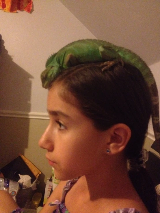 girl with green lizard on her head looking into mirror