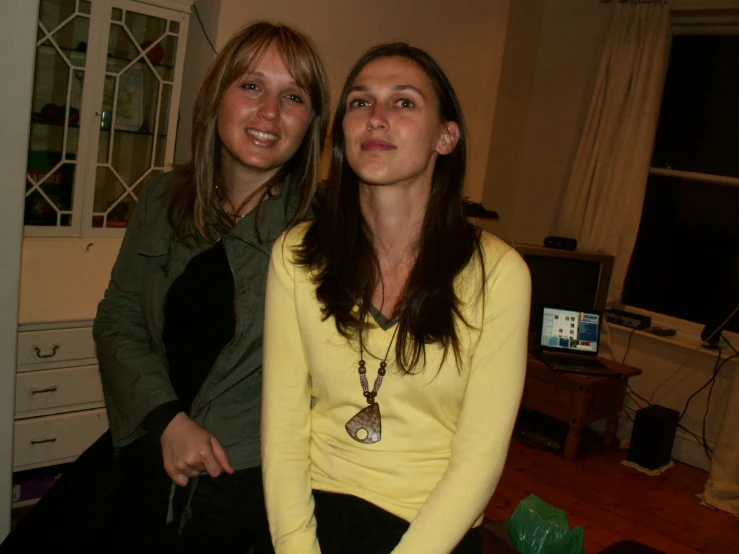 two woman smile brightly in the dark while they sit together