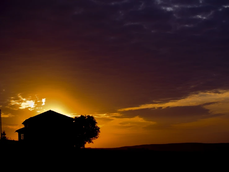 the sun is setting behind a house with a horse standing on the lawn