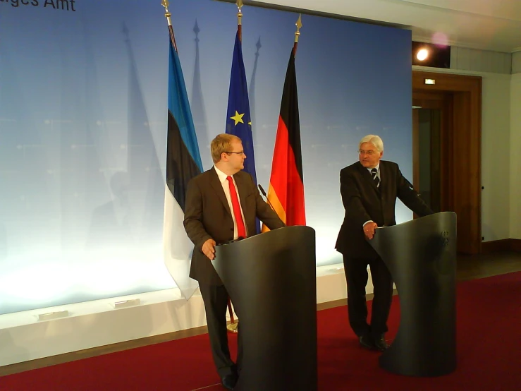 two men are standing in front of a podium with two flags