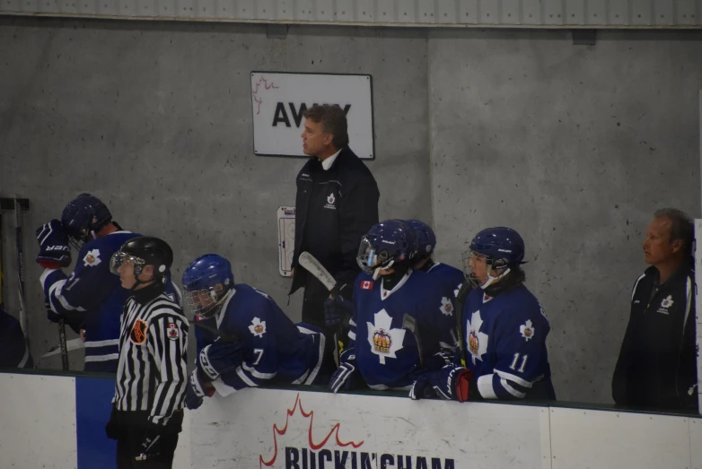 a hockey coach stands at the bench as his team gets ready