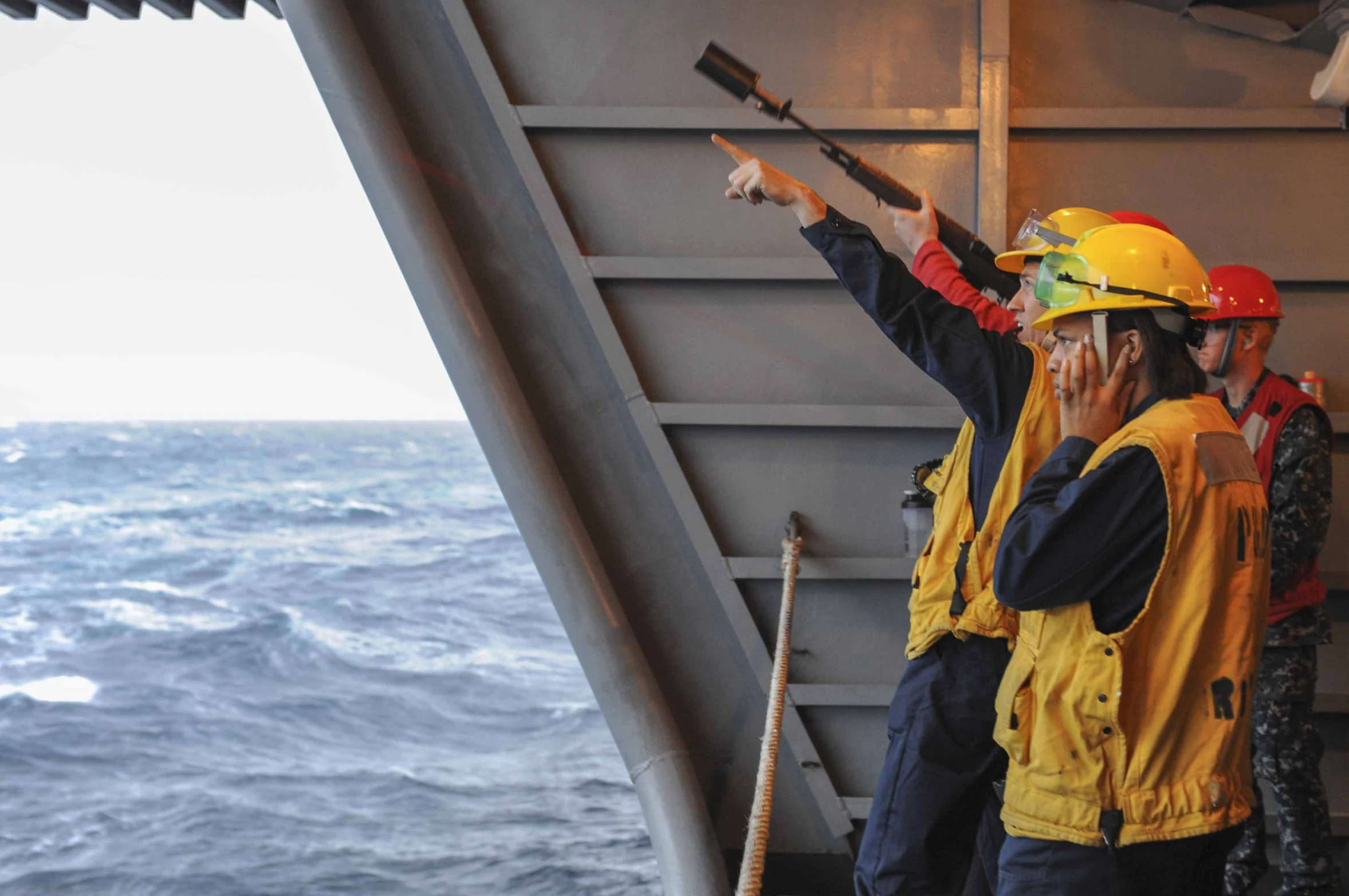 three men wearing yellow helmets and safety gear standing on the deck of a ship