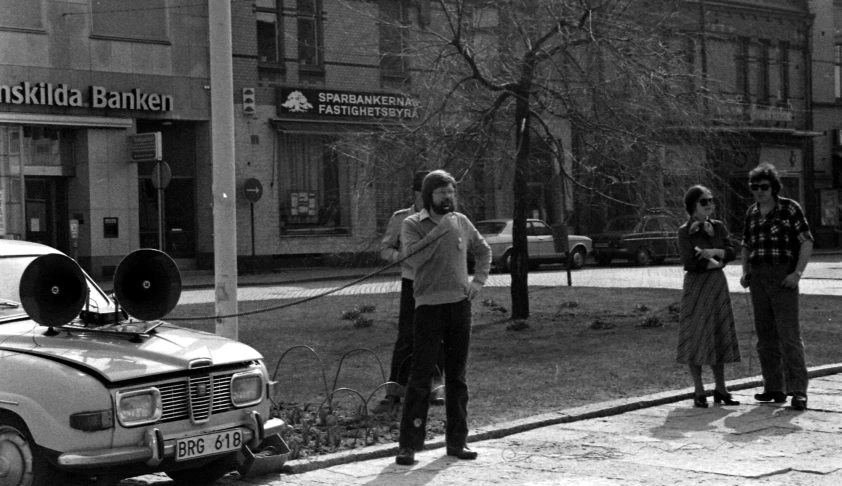 three men and a woman standing on the sidewalk next to each other