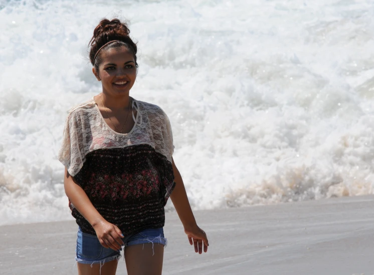 a young woman standing on a beach with her hands in the air