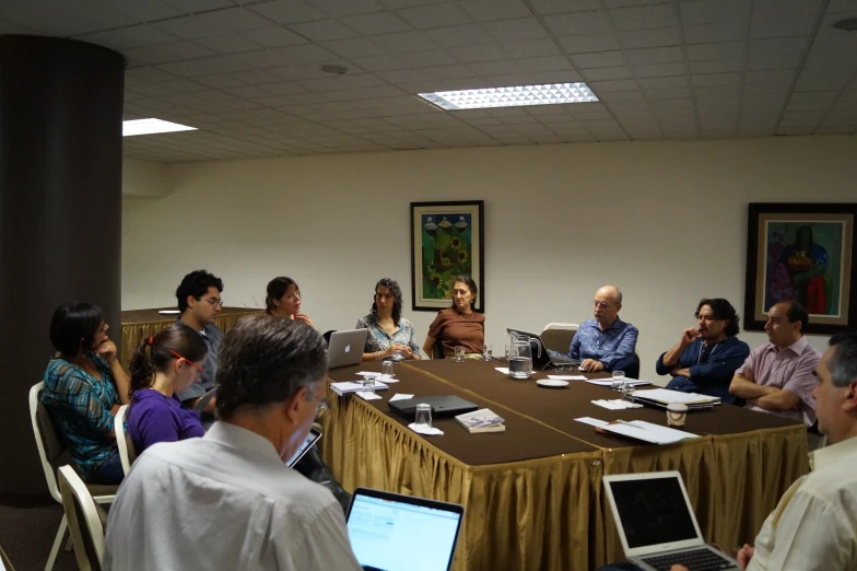 several men and women sitting around a table with laptops