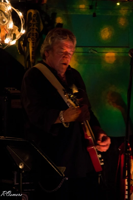 a man with glasses plays his guitar in front of several other instruments