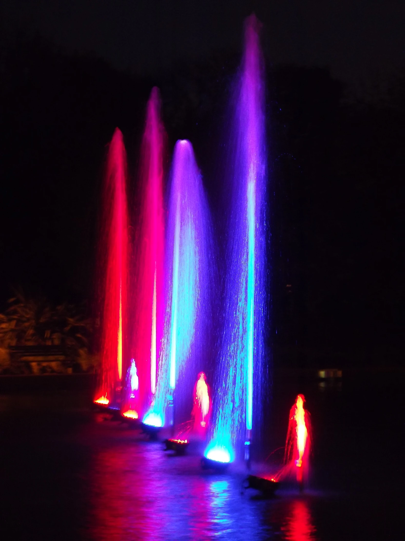 a large fountain with colorful lights on the water at night