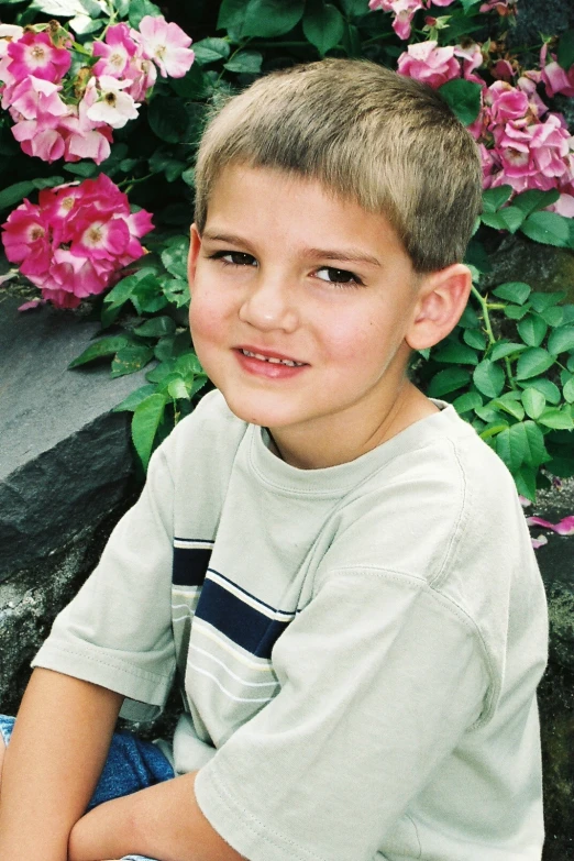 a boy sits in front of some pink flowers