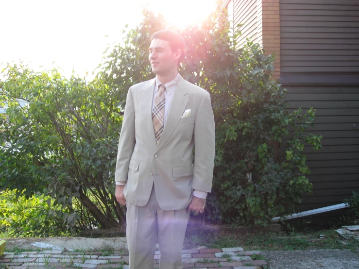 man in beige suit standing in front of tree