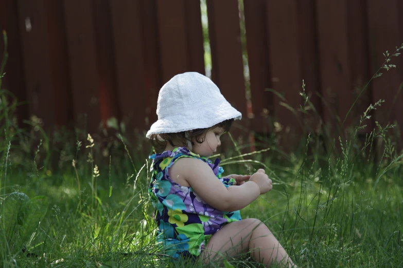 a young child wearing a sunhat is sitting in the grass