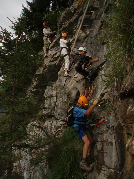 three men climb a large rocky outcrop