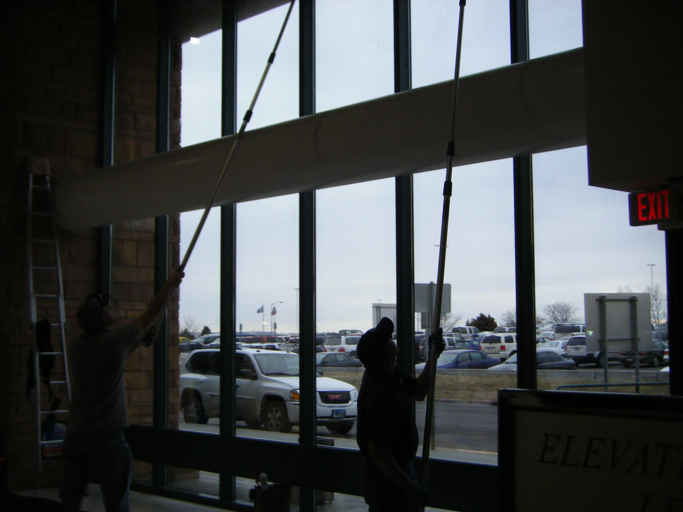 two men install glass windows in a car dealership