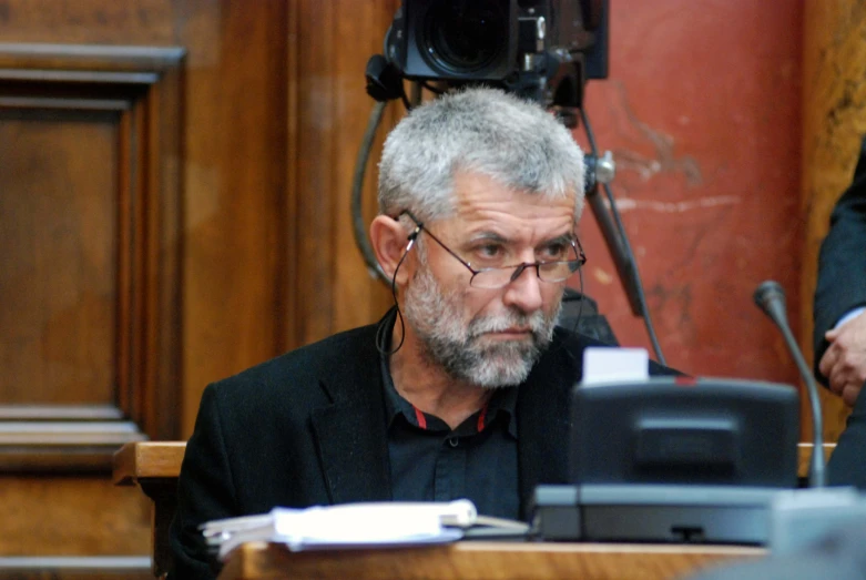 a bearded man is sitting at a courtroom table