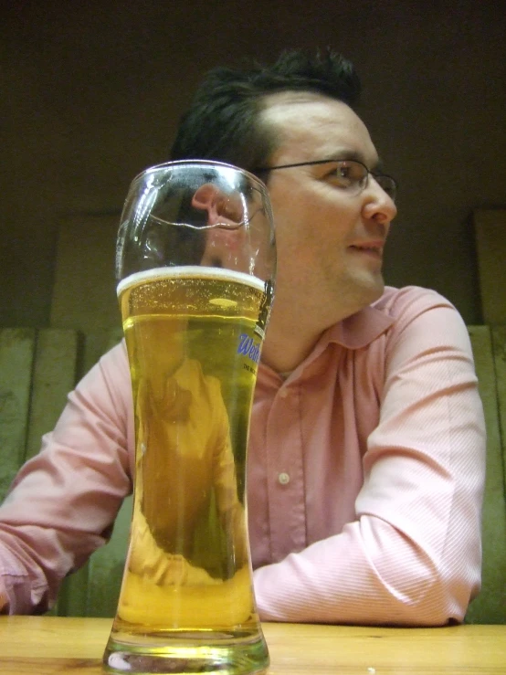 a man is sitting at a wooden table and resting his head on a beer glass