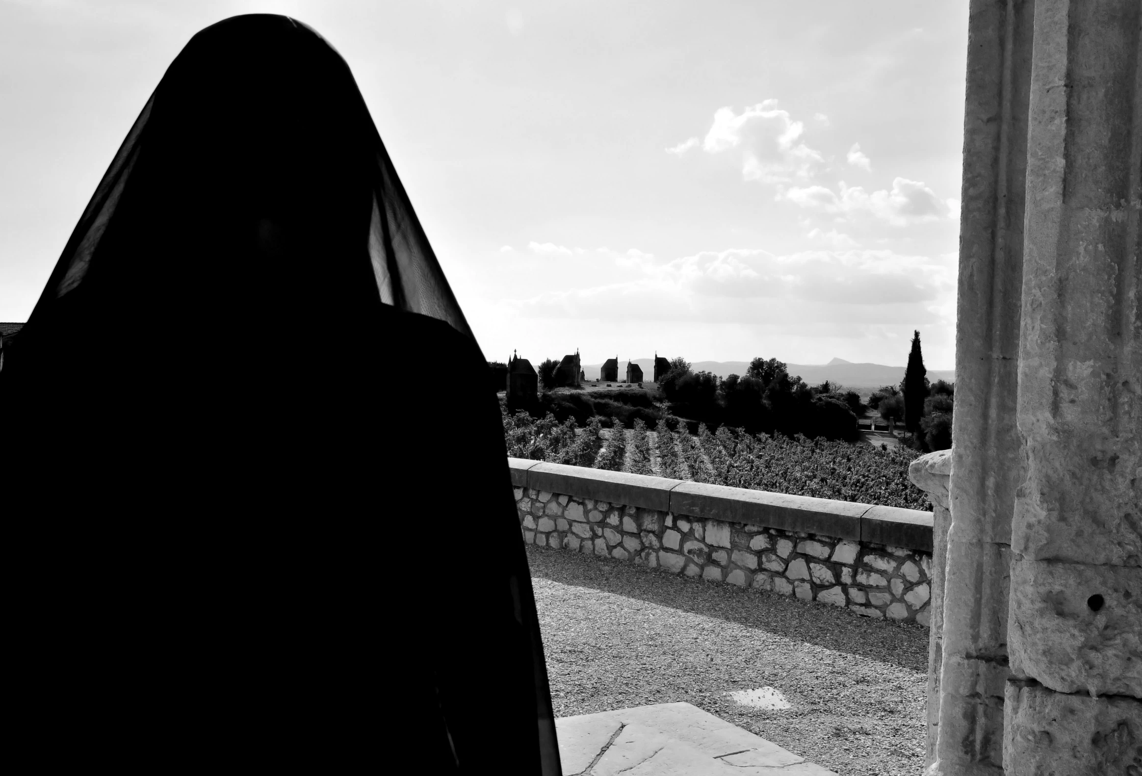 an older fashion woman wearing black in front of a stone building