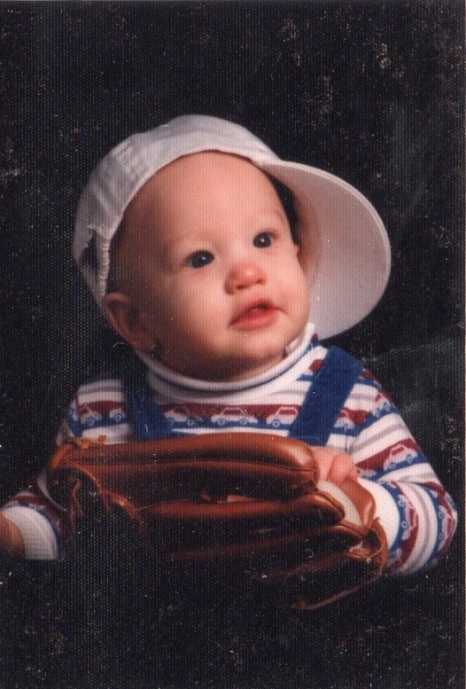 a baby in a white hat is holding a glove