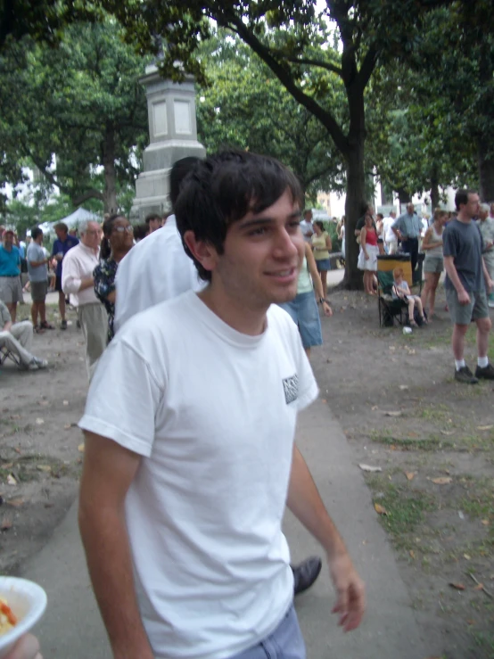 man in white shirt standing outside near people eating