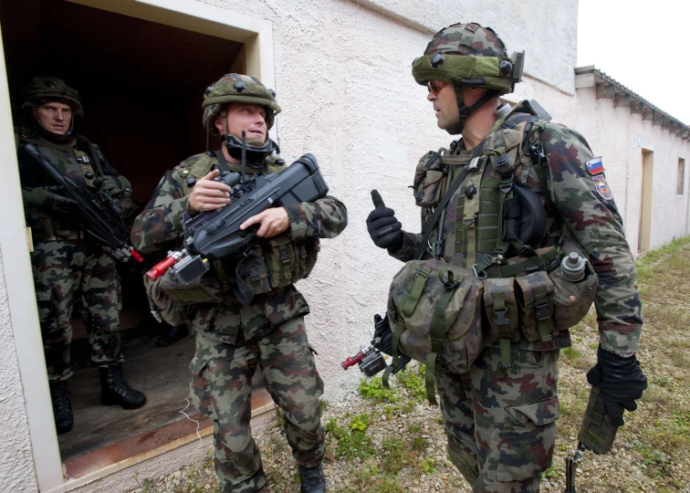 soldiers dressed in camouflage holding guns standing outside a building