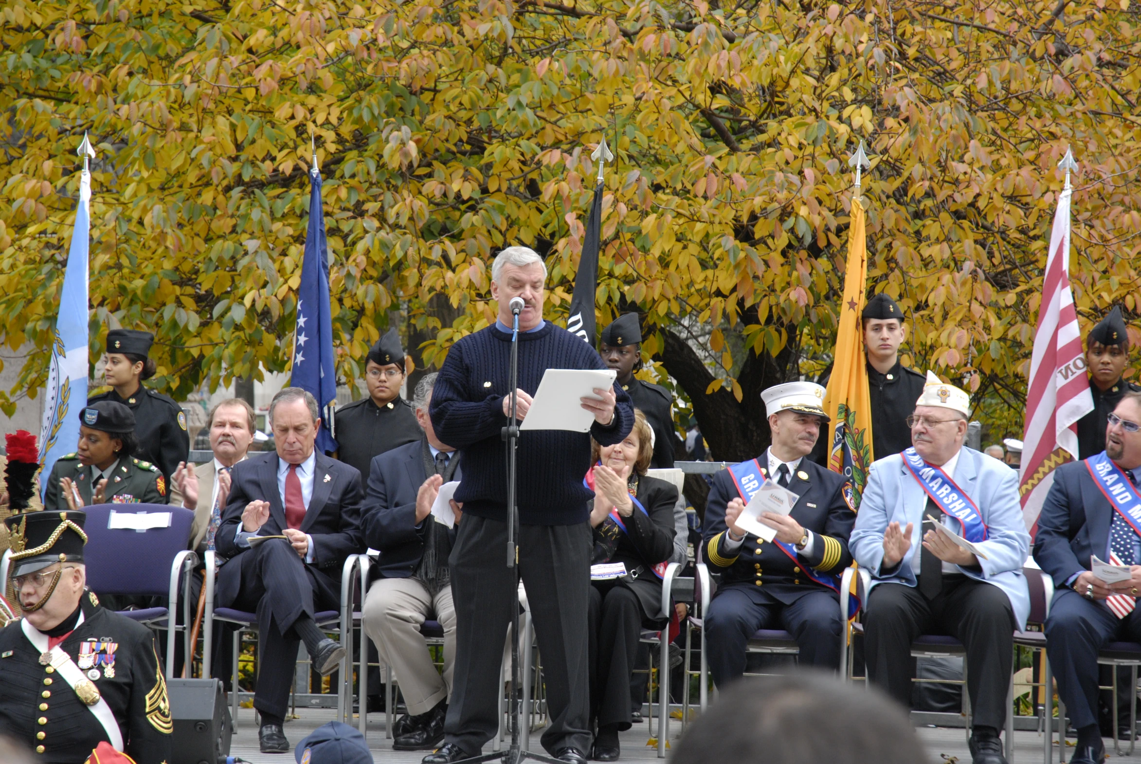 a person giving a speech with military men in the background