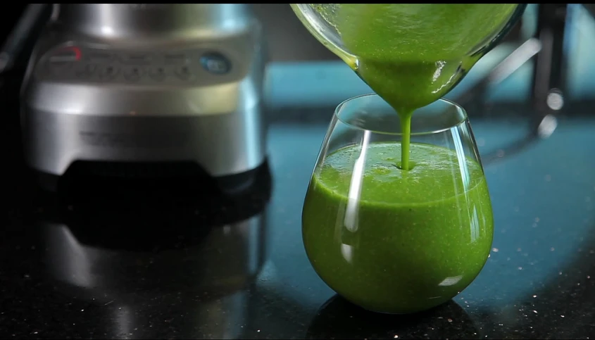 a blender is pouring a green juice in it