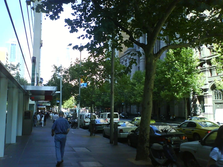 people walk down a sidewalk near parked cars