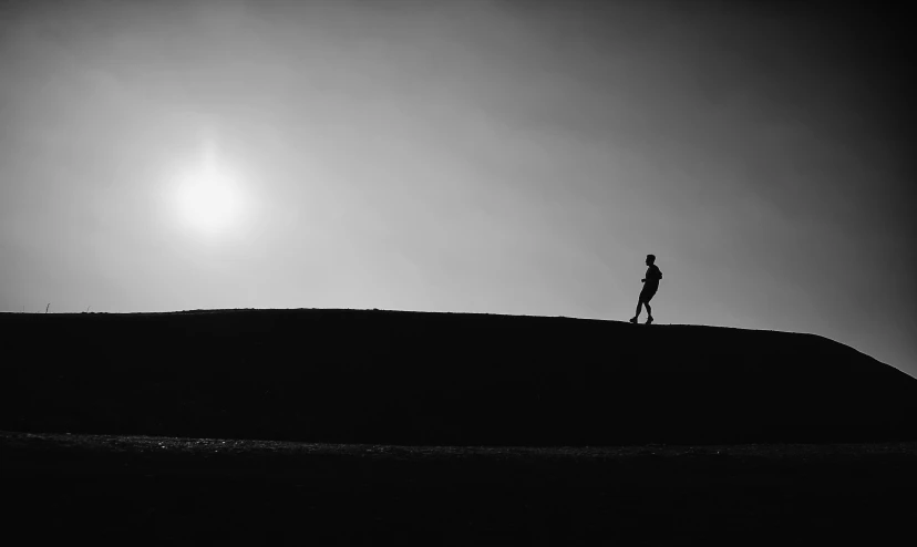 man standing alone on top of hill watching the sun