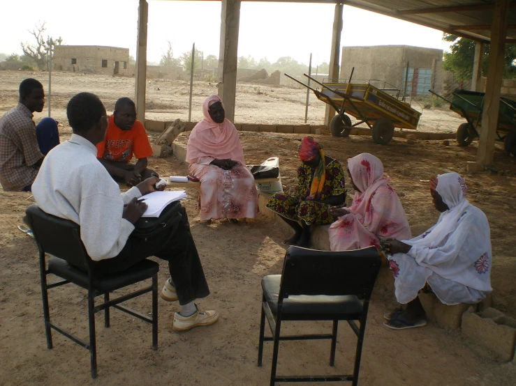 several people gathered in the shade and sitting in chairs