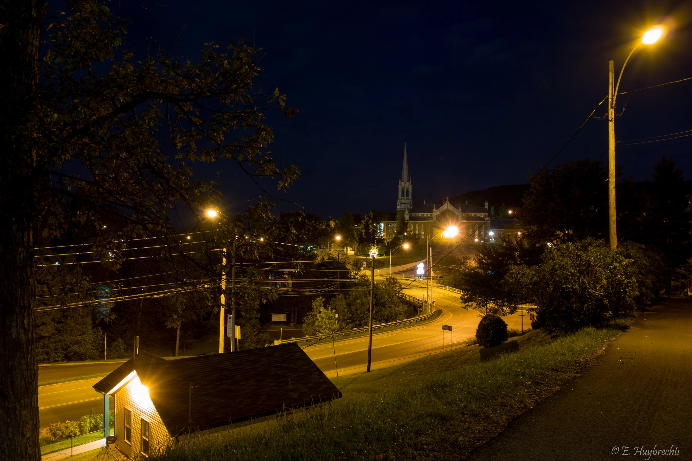 a night time cityscape with a light pole over the street and small houses