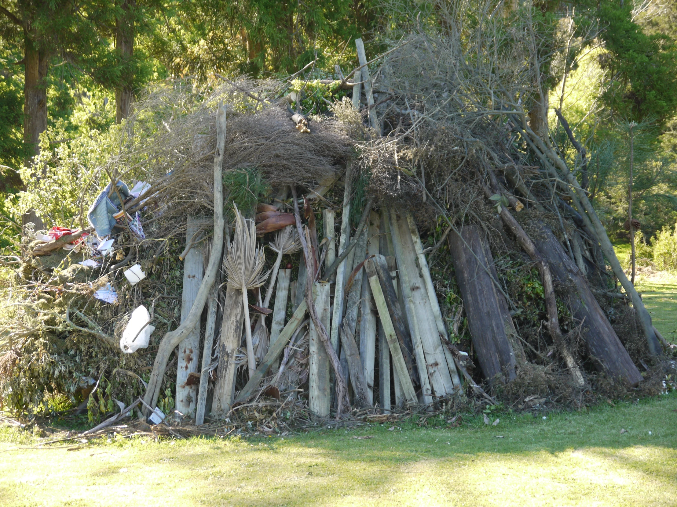 an old pile of wood sitting on top of a lush green field