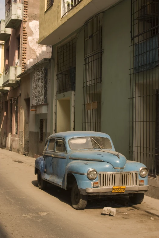 an old, dusty blue car sits on the side of the road next to some buildings