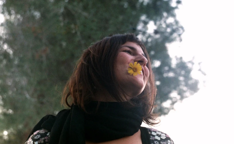 a woman in a scarf holding a flower up to her mouth