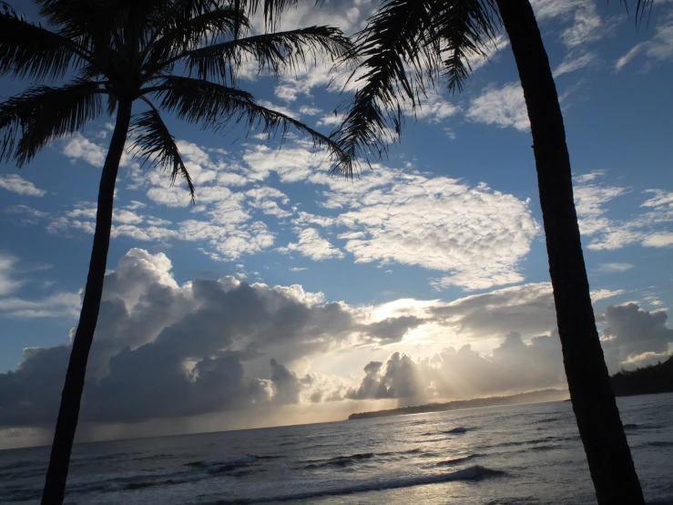 the sun breaking through the clouds above a beach